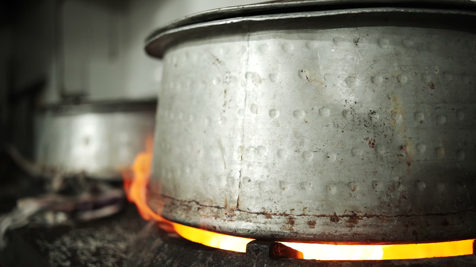 A sealed steel handi over an open flame, the ring of fire visible beneath its rim